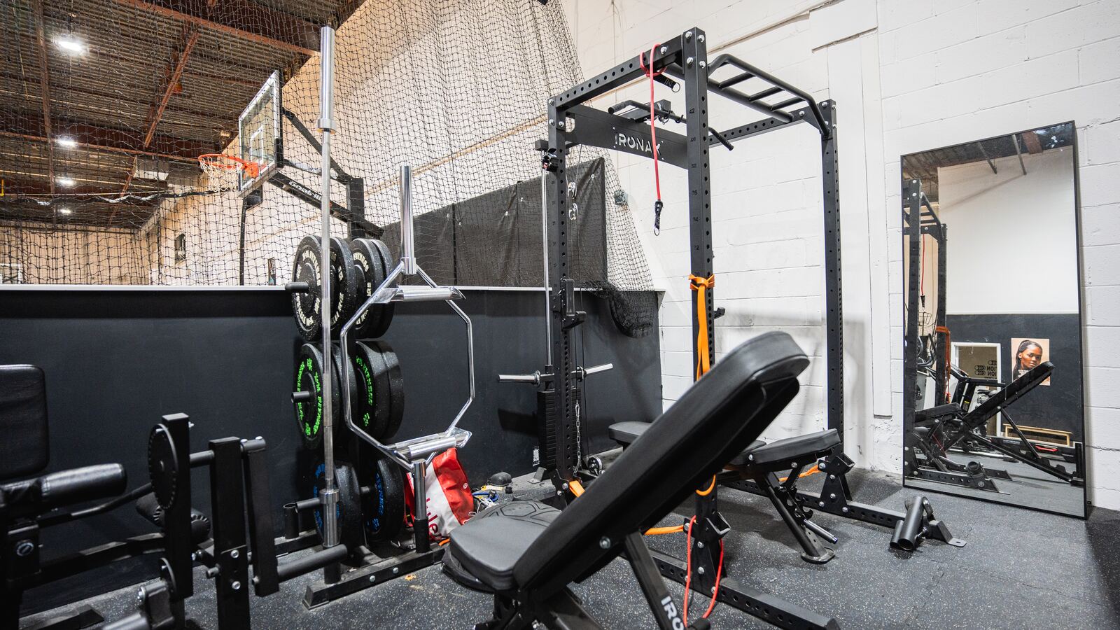 Power rack with pull-up bar and cable attachment beside an adjustable bench and a full-length mirror