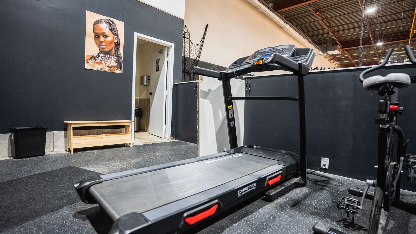 Treadmill and spin bike on rubber flooring beside the washroom entrance